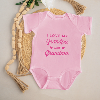 Pink baby onesie with 'I love my grandpa and grandma' text on a neutral background