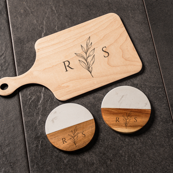 Wooden cutting board with 'R S' monogram and two round coasters with the same design on a dark surface.
