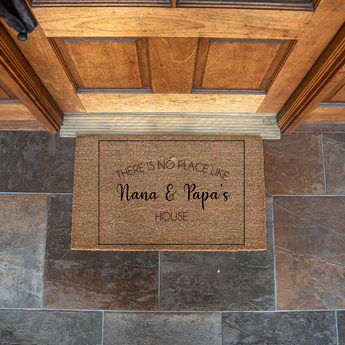 Doormat with text 'There is no place like Nana & Papa's House' on a stone floor.