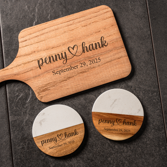 Wooden paddle and coasters with engraved names and date on a dark surface