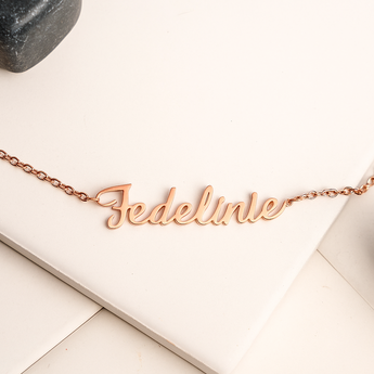 Rose gold necklace with 'Federlinie' engraving on a light wooden surface.