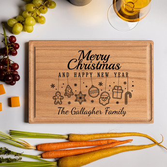 A personalized cutting board made from smooth oak wood engraved with “Merry Christmas and Happy New Year” above festive hanging icons including a gingerbread man, tree, star, ornament, Santa face, present, and candy cane. The board features “The Gallagher Family” in elegant script and is styled with grapes, cheddar cubes, a glass of golden wine, and colorful heirloom carrots. This custom cutting board is a beautiful Christmas gift idea and a functional holiday cutting board gift for families and hosts.