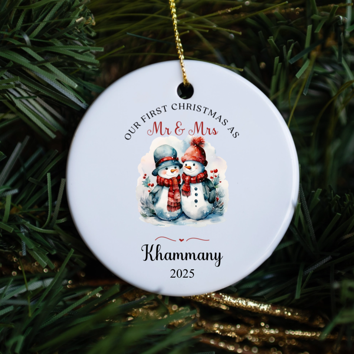 Round Christmas ornament with snowmen and text 'Our First Christmas as Mr & Mrs' on a green pine branch.